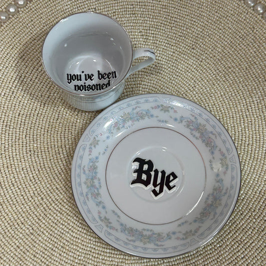 Teacup and saucer set with 'you've been' and 'Bye' text on a textured surface